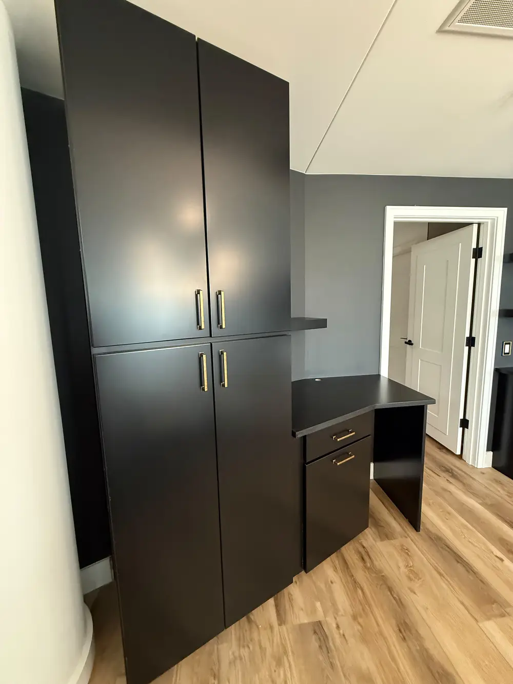 Custom matte black pantry cabinets and integrated built-in desk designed by Evolve Design for the SW River Parkway project in Portland. Features modern gold hardware and warm wood flooring