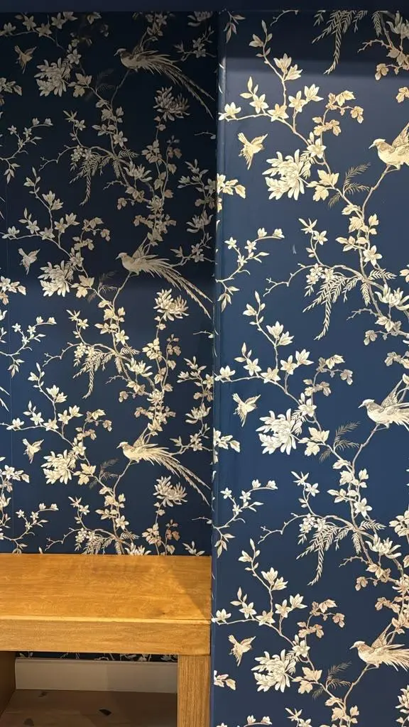 Custom entryway nook designed by Evolve Design for the SW 14th St project in Gresham, Oregon. Features an elegant navy blue wallpaper with a metallic gold bird and floral pattern, paired with a natural wood floating bench