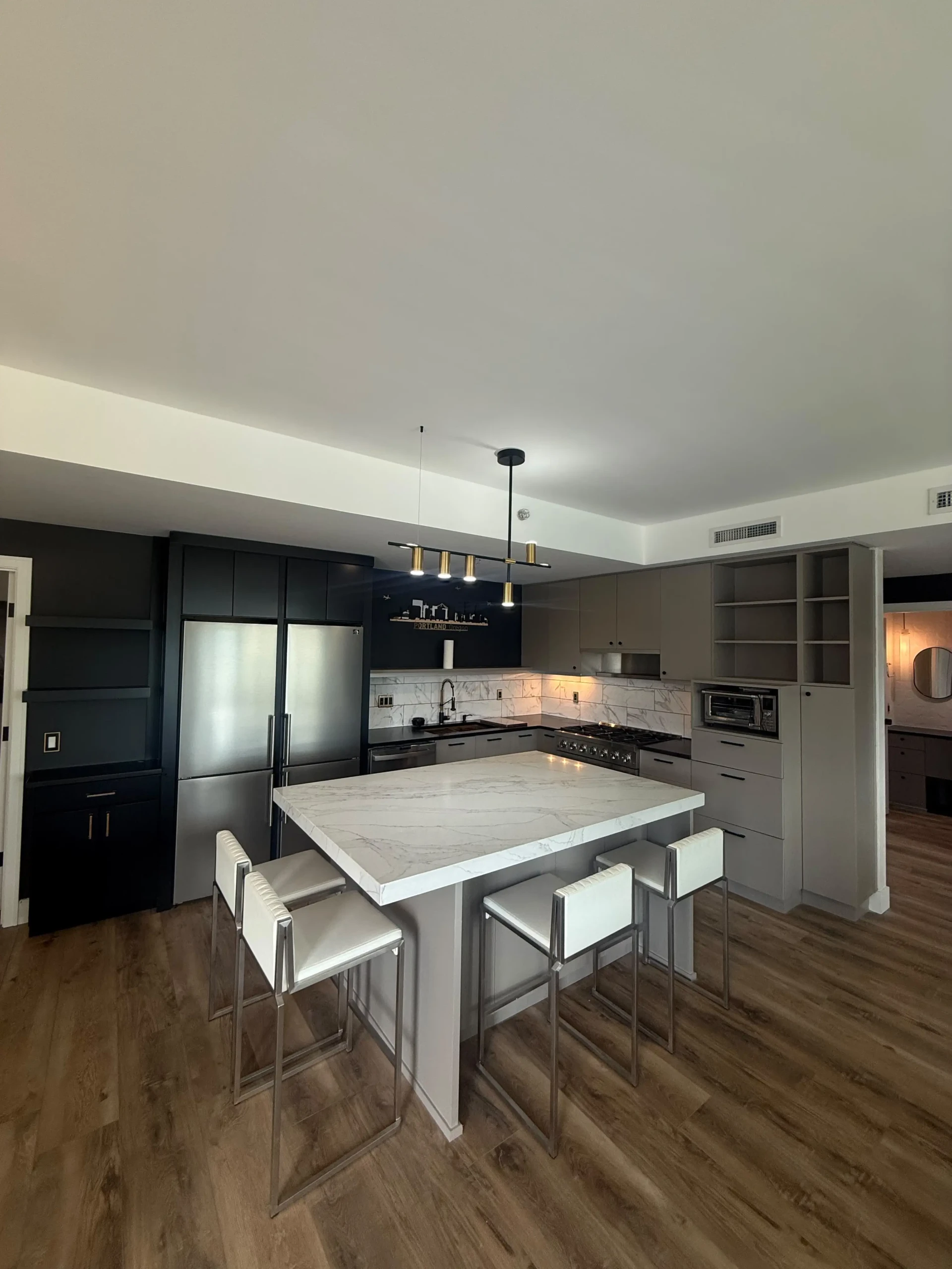 Modern kitchen remodel by Evolve Design at the SW River Parkway project in Portland. Features a white marble island with bar stools, stainless steel appliances, and contemporary grey and black cabinetry.