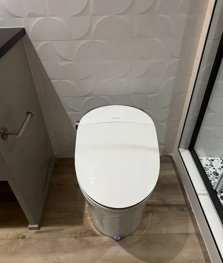 Close-up view of a sleek modern toilet with an integrated smart bidet seat installed by Evolve Design at the SW River Parkway project in Portland. The bathroom features textured geometric wall tiles and wood-look flooring
