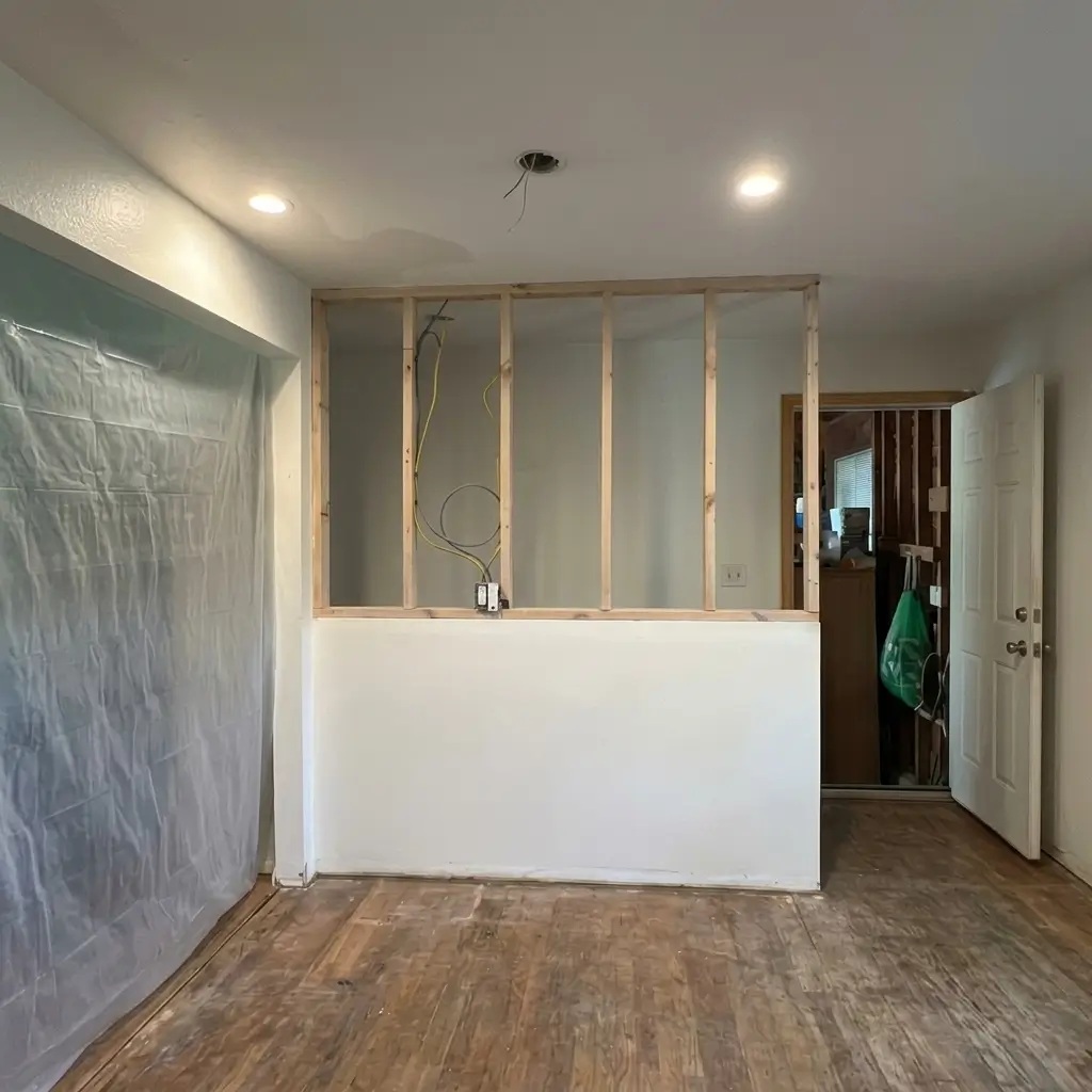 Open half-wall wood stud framing with exposed electrical wiring and plastic containment sheeting during an interior home remodel by Evolve Design