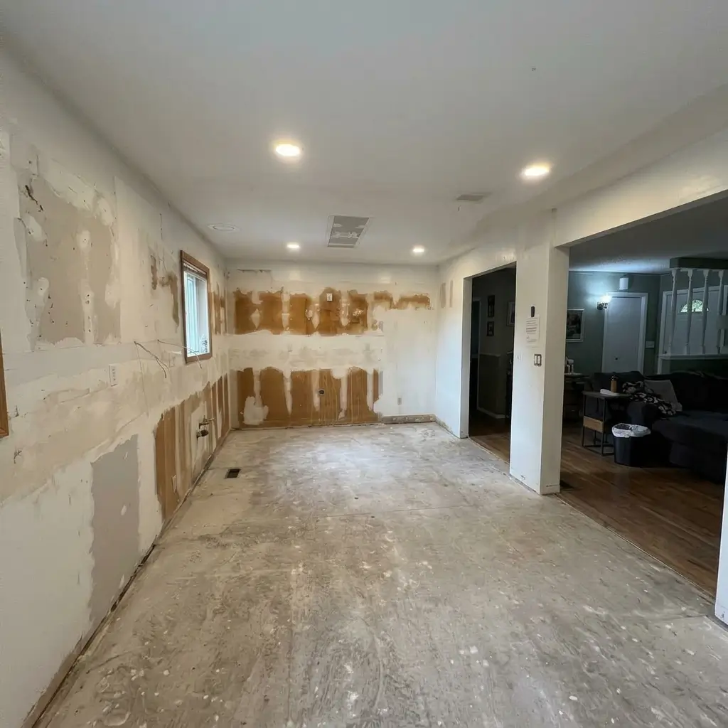 Gutted kitchen space during demolition phase with removed cabinets, exposed wall backing, and bare concrete subfloor in an Evolve Design renovation project