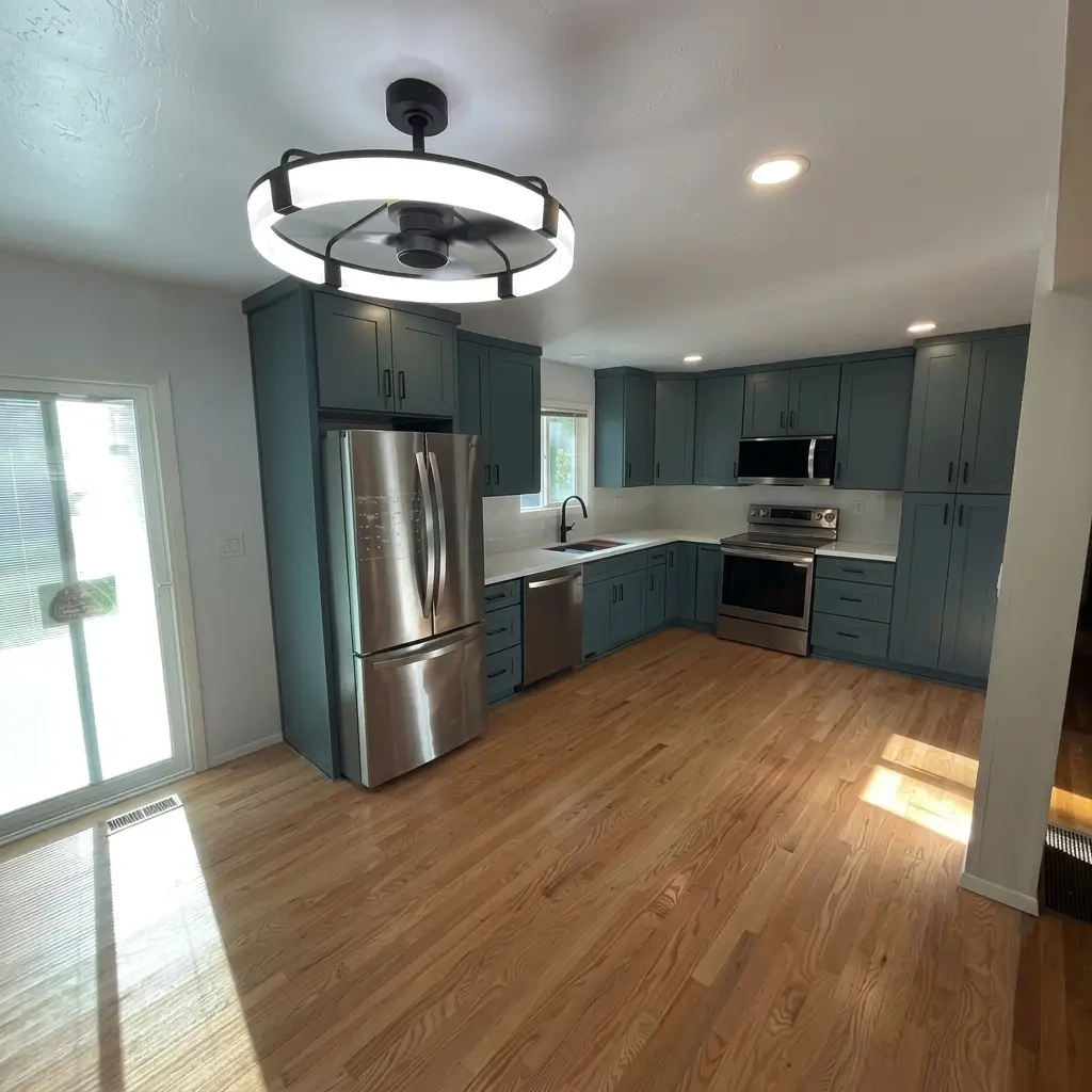 Wide angle of completed kitchen remodeling project in Damascus, Oregon, showing modern circular ceiling fan light fixture, dark teal cabinets, stainless steel refrigerator, and refinished hardwood floors