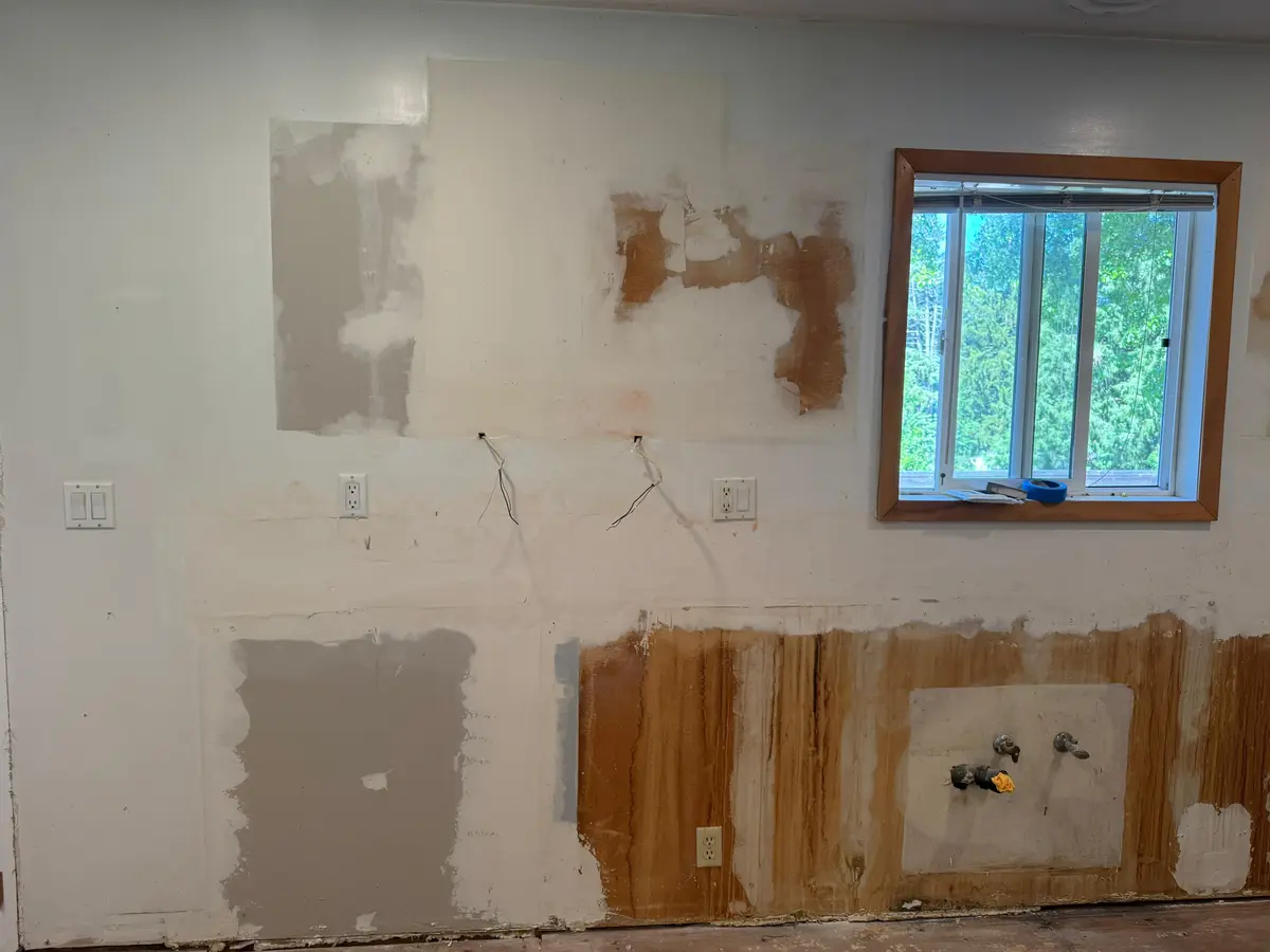 Kitchen wall undergoing demolition during a kitchen remodeling project in Damascus, Oregon, showing exposed drywall, wiring, and plumbing connections next to a window