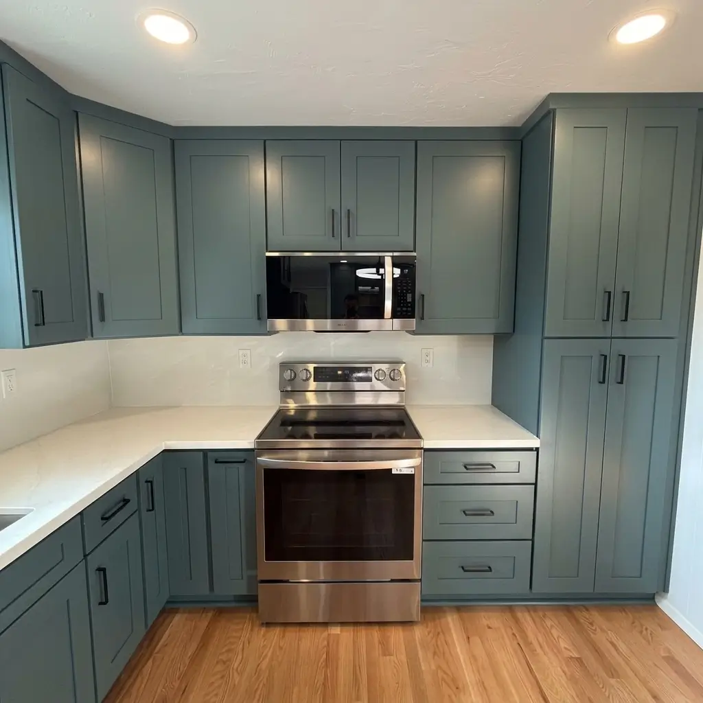 Completed kitchen remodeling transformation in Damascus, Oregon, featuring dark teal cabinetry, stainless steel range and microwave, white quartz counter, and natural hardwood floor