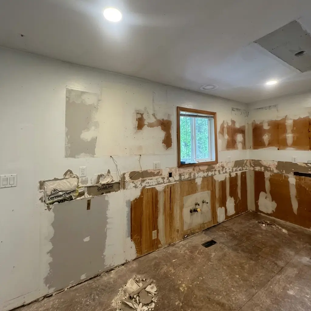 Wide shot of a kitchen undergoing complete demolition during a kitchen remodeling project in Damascus, Oregon, showing stripped walls, exposed insulation, plumbing hookups, and subfloor debris