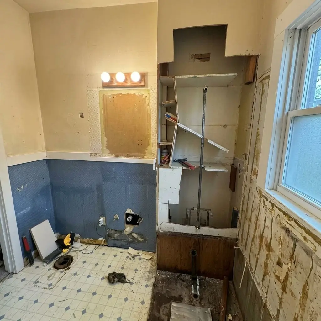 Mid-renovation demolition view of a Portland bathroom showing exposed plumbing pipes, removed drywall, stripped tile walls, and gutted bathtub area