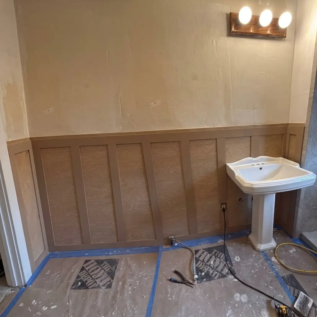 Unfinished wood board-and-batten wainscoting installation on bathroom wall next to a pedestal sink during construction in Portland