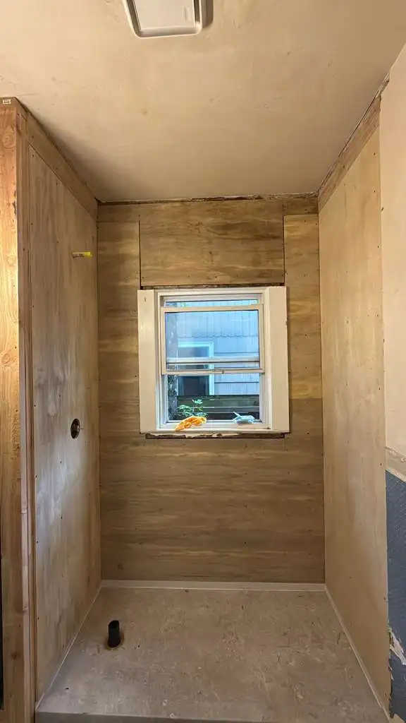 Plywood backing and shower pan framing surrounding a window during the rough-in construction phase of a bathroom remodel in Portland