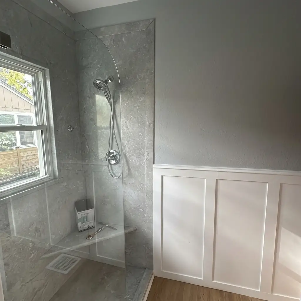 Corner view of a tiled walk-in shower with a built-in bench, curved glass partition, window, and adjacent white board-and-batten wainscoting wall paneling in a Portland bathroom